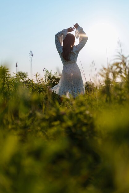 Vue arrière d'une femme en robe blanche dans un champ au coucher du soleil