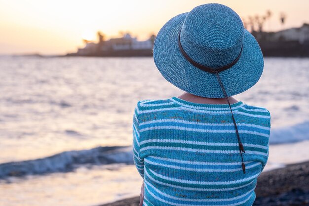 Vue arrière d'une femme senior caucasienne détendue assise sur la plage profitant de l'heure d'or du coucher du soleil femme profitant de vacances de temps libre ou de retraite