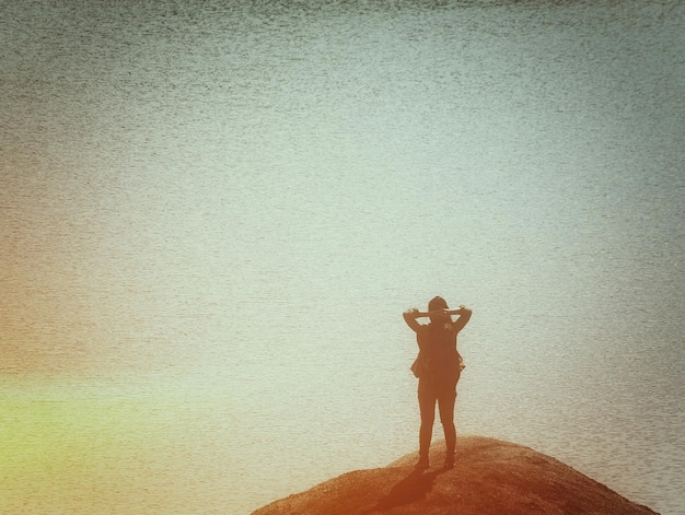 Photo vue arrière d'une femme en silhouette debout sur un rocher près de la mer
