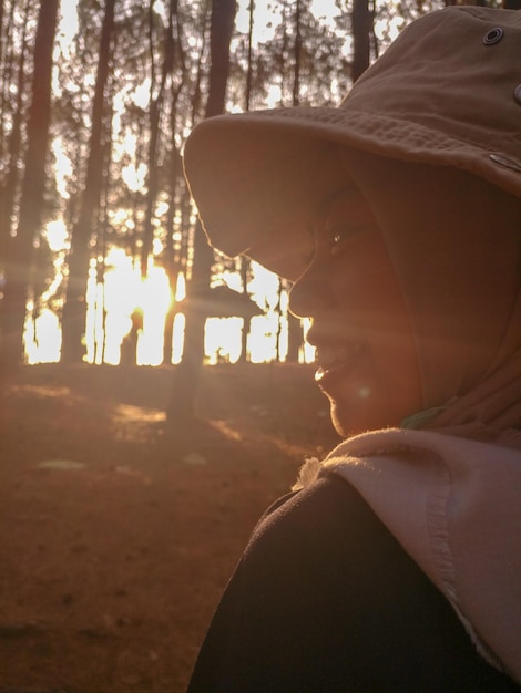 Photo vue arrière d'une femme souriante portant un chapeau dans la forêt au coucher du soleil