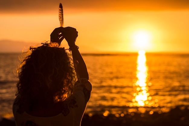 Photo vue arrière d'une femme tenant une plume sur la plage au coucher du soleil