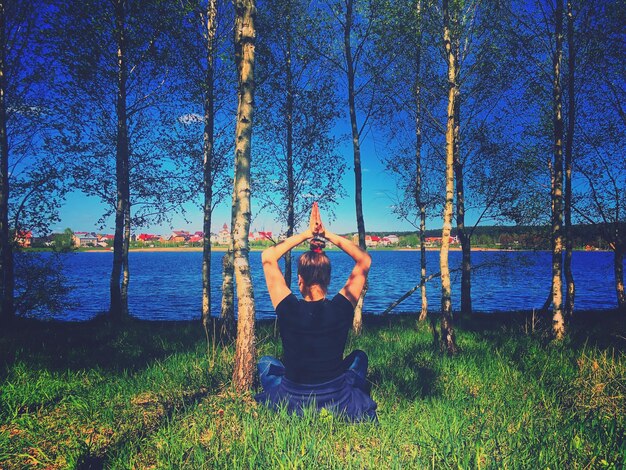 Photo vue arrière d'une femme en train de méditer assise sur un champ herbeux près d'un lac dans la forêt