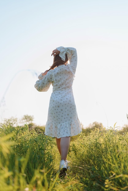 Photo vue arrière d'une femme vêtue d'une robe blanche dans un champ au coucher du soleil