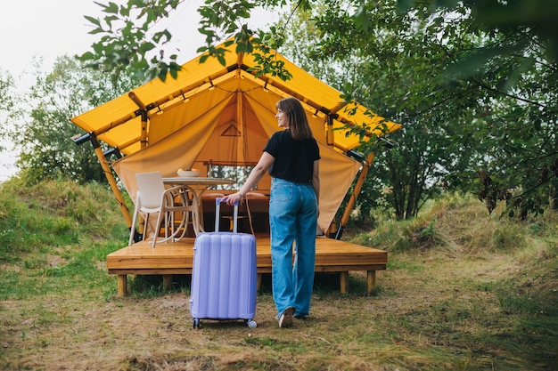 Vue arrière d'une femme voyageuse avec des bagages se déplaçant vers la chambre d'une maison de glamping confortable Tente de camping de luxe pour les vacances d'été en plein air et les vacances Concept de style de vie