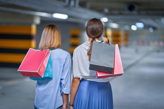 Vue arrière des femmes avec des sacs à provisions dans un parking souterrain