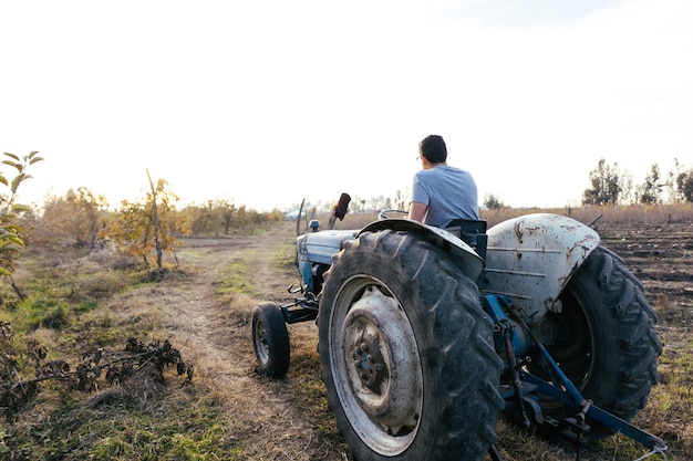 Vue arrière d'un fermier latin conduisant un vieux tracteur, au milieu de ses terres agricoles au coucher du soleil