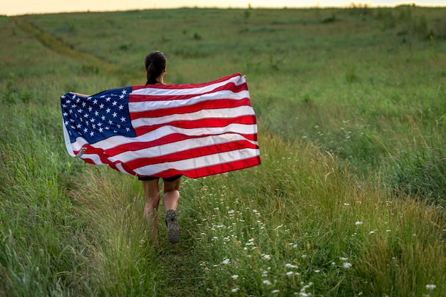 Vue arrière d'une fille avec un drapeau américain courant sur l'herbe dans le domaine