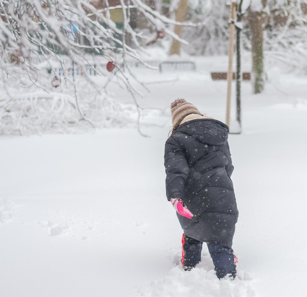 Vue arrière d'une fille marchant avec beaucoup de difficulté dans la neige profonde.