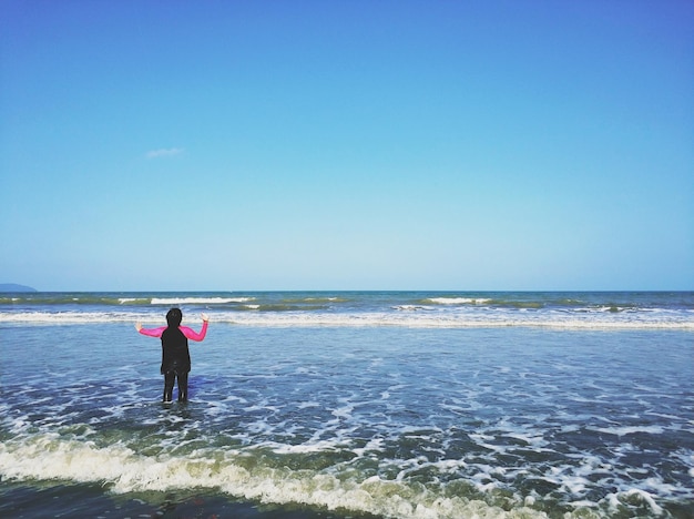 Photo vue arrière d'une fille sur la plage contre un ciel bleu clair