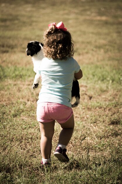 Photo vue arrière d'une fille tenant un chien en marchant sur un champ herbeux