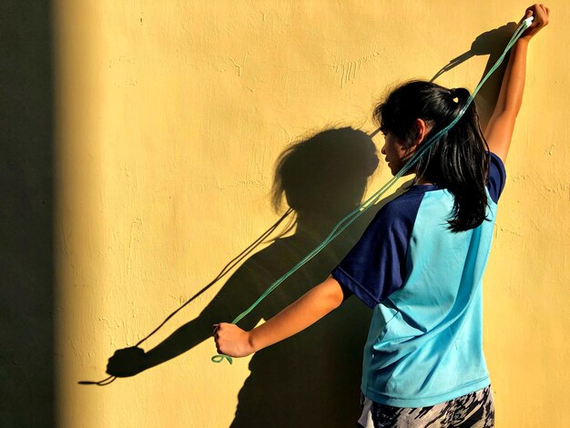 Photo vue arrière d'une fille tenant une corde de saut contre le mur