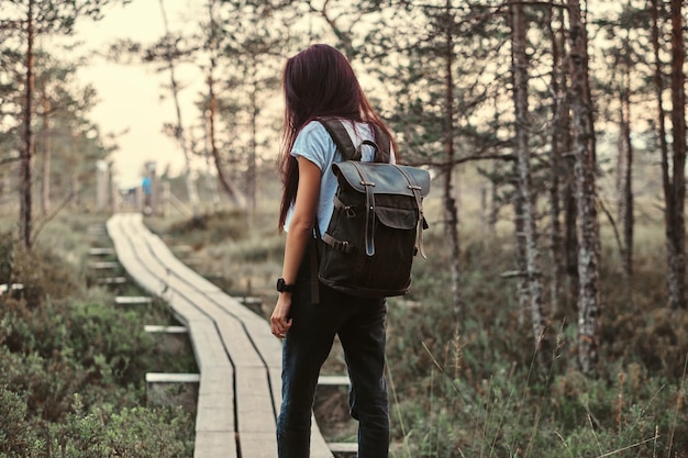 Vue arrière d'une fille touristique avec sac à dos à pied sur un sentier en bois dans une belle forêt.