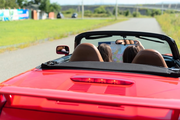 Vue arrière de filles heureuses conduisant une voiture cabriolet rouge pendant un voyage de vacances en s'amusant ensemble en découvrant de nouveaux endroits en regardant la carte Voyage en voiture en profitant du concept de liberté Mise au point sélective