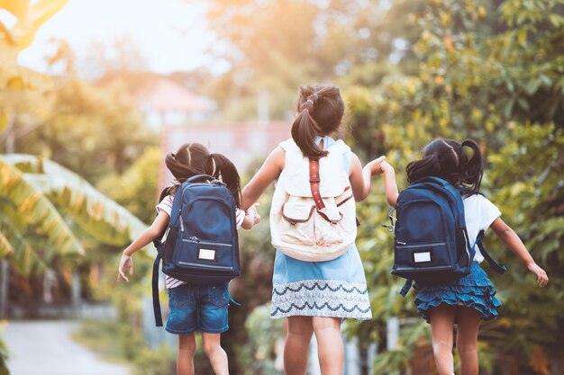 Photo vue arrière de filles avec des sacs à dos tenant la main en marchant sur la route