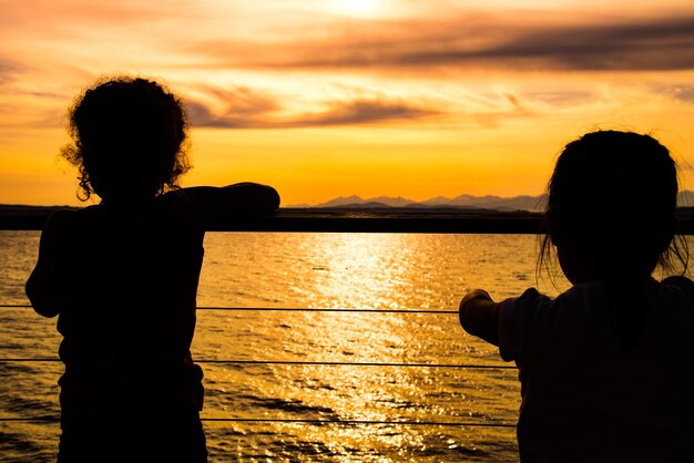 Photo vue arrière de filles en silhouette regardant la mer au coucher du soleil