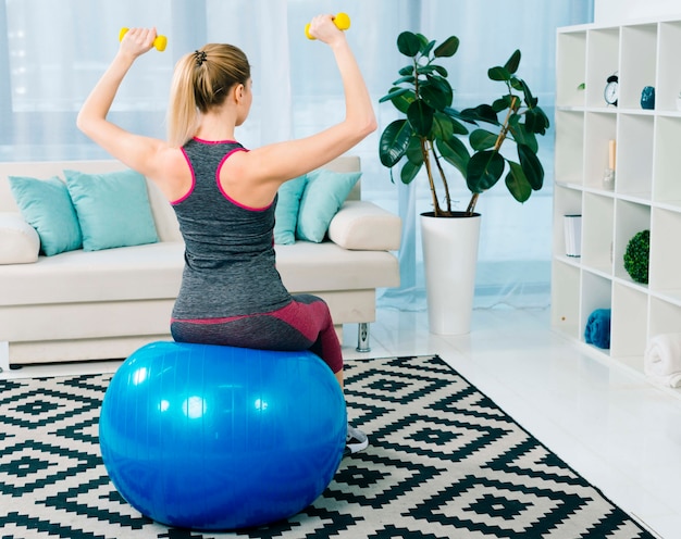 Photo vue arrière, de, fitness, jeune femme, séance, sur, bleu, pilates, balle, exercer, à, haltères jaune