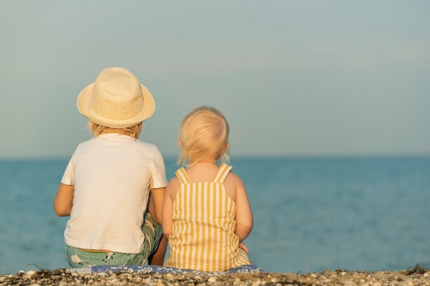 Vue arrière frère et soeur sont assis sur la plage et regardant la mer