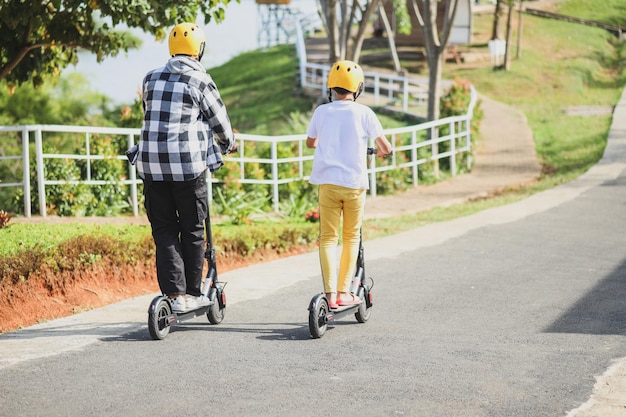 Vue arrière d'un frère en vacances s'amusant à conduire un scooter électrique dans le parc de la rue. Jeunesse