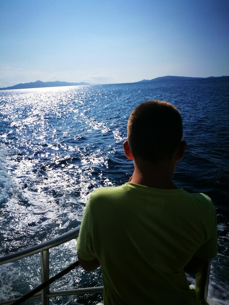 Photo vue arrière d'un garçon regardant la mer contre le ciel pendant une journée ensoleillée