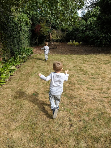 Vue arrière de garçons jumeaux courant sur l'herbe contre les arbres