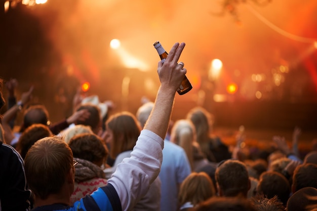 Vue arrière d'un gars dans un public saluant le groupe sur scène lors d'un festival de musique