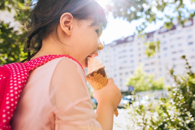 Vue arrière gros plan portrait d'une jolie petite fille marchant le long de la rue de la ville et mangeant des glaces en plein air