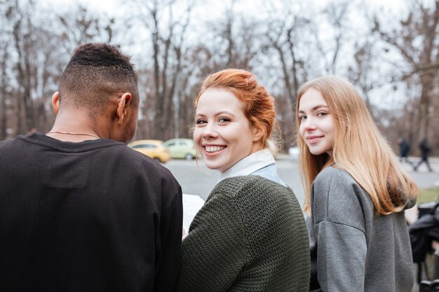 Vue arrière d'un groupe de jeunes adolescents souriants assis ensemble à l'extérieur