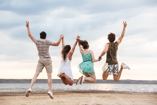 Vue arrière d'un groupe de jeunes amis joyeux sautant à la plage