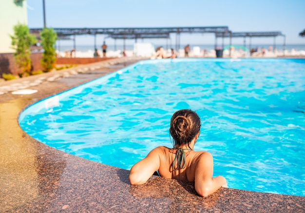 Vue arrière happy little teenage girl se pencha sur le bord de la piscine et bénéficie d'une eau chaude et propre