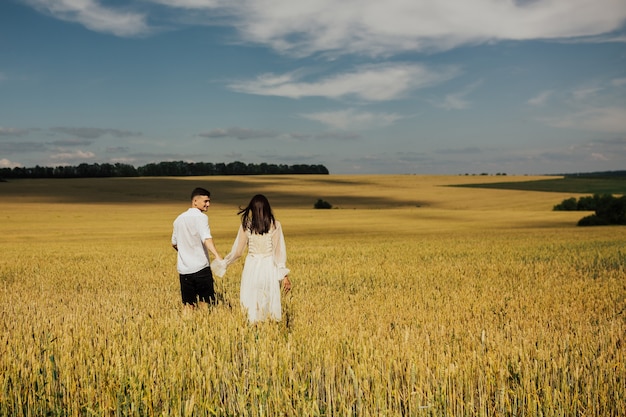 Vue arrière de l'heureux jeune couple marchant ensemble dans le champ de blé.