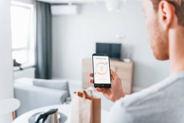 Vue arrière d'un homme adulte qui contrôle à l'intérieur la technologie de la maison intelligente