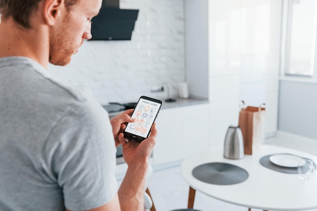 Vue arrière d'un homme adulte qui contrôle à l'intérieur la technologie de la maison intelligente