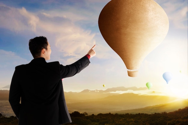 Vue arrière d'un homme d'affaires asiatique pointant un ballon à air coloré volant avec un fond de ciel coucher de soleil