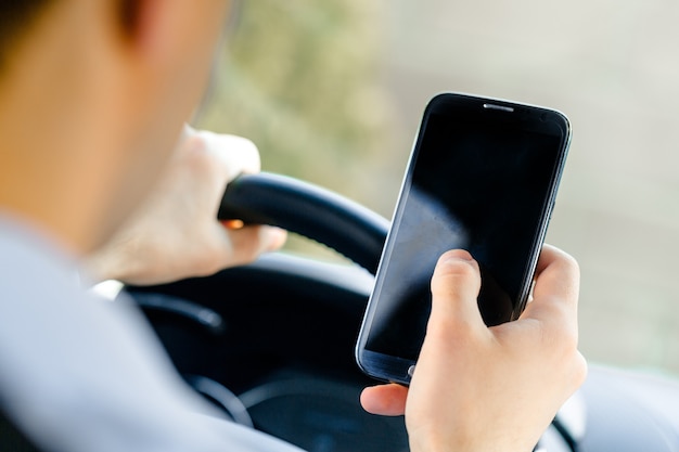 Vue arrière de l'homme assis au siège du conducteur de la voiture et regardant l'écran noir du smartphone