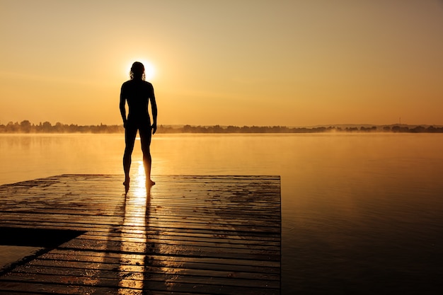 Photo vue arrière de l'homme athlétique debout sur la jetée en bois et se préparer à nager au lac pendant le lever du soleil d'été.