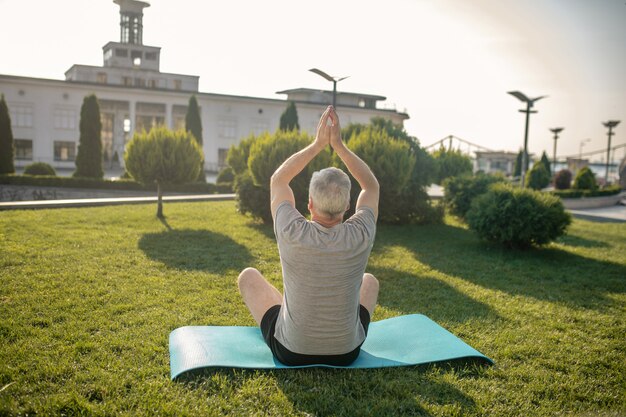 Vue Arrière De L'homme Aux Cheveux Gris Pratiquant Le Yoga à L'extérieur, Levant Les Mains Au-dessus De La Tête