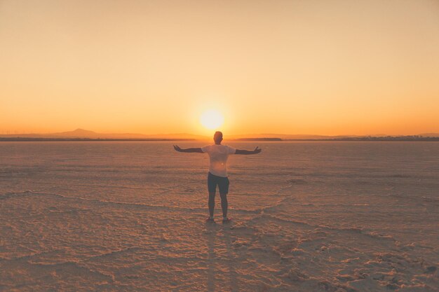 Photo vue arrière d'un homme avec les bras tendus debout au sel plat contre le ciel au coucher du soleil