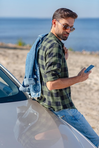 Vue arrière d'un homme caucasien qui envoie des SMS au téléphone tout en se tenant à la voiture