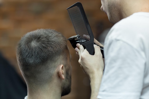 Photo vue arrière - un homme de coiffure avec des outils a coupé un jeune homme inconnu dans un salon de coiffure