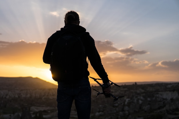 Vue arrière de l'homme debout contre le lever du soleil avec un drone à la main