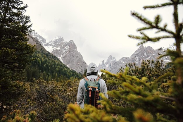 Photo vue arrière d'un homme debout dans la forêt contre des montagnes enneigées