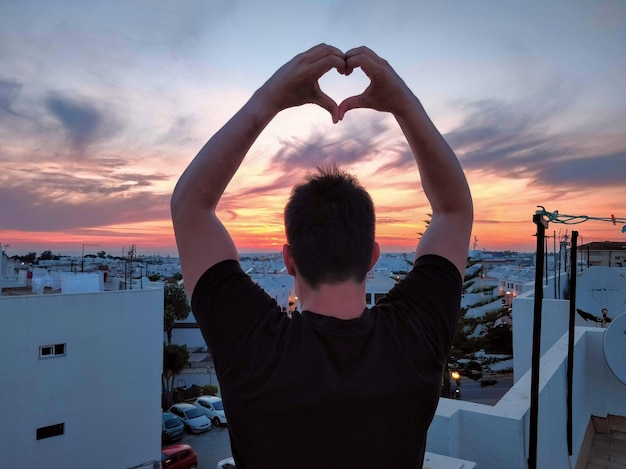 Vue arrière de l'homme debout dans la mer contre le ciel coucher de soleil