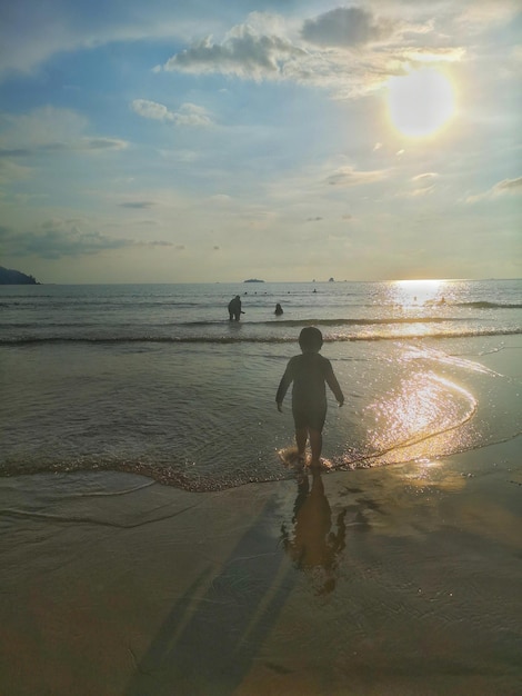 Vue arrière d'un homme debout sur la plage contre le ciel au coucher du soleil