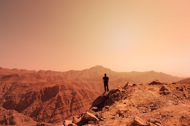 Photo vue arrière d'un homme debout sur un rocher contre le ciel au coucher du soleil