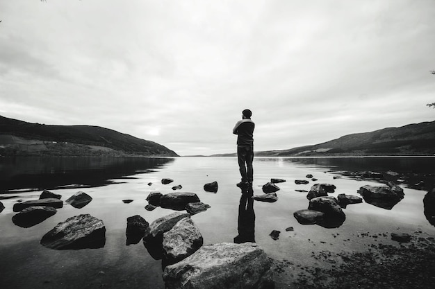 Photo vue arrière d'un homme debout sur un rocher dans un lac contre le ciel