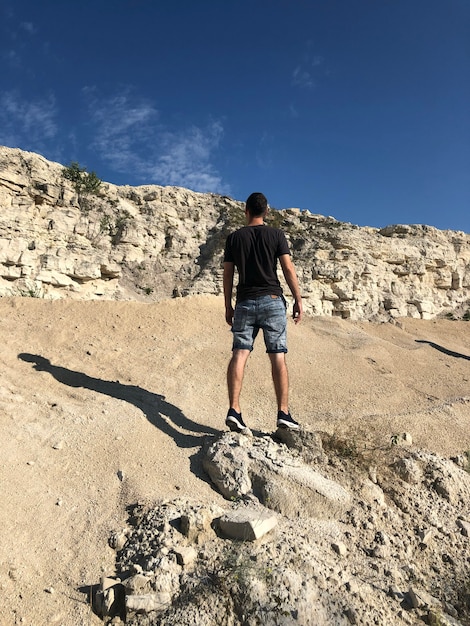 Vue arrière de l'homme debout sur le rocher sur le magnifique paysage du ciel clair avec des rochers blancs et des collines avec des arbres