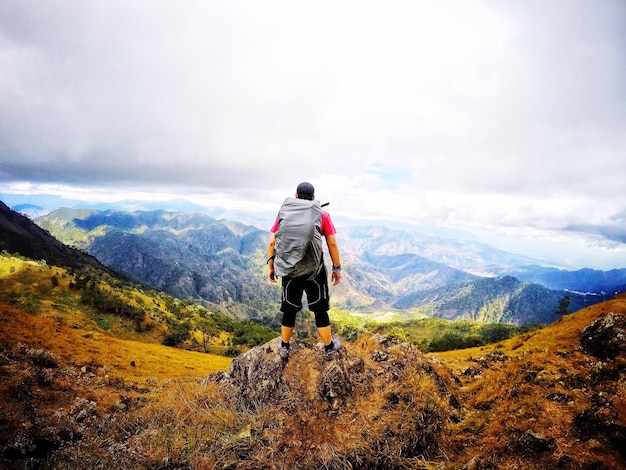 Vue arrière d'un homme debout sur le sommet d'une montagne contre un ciel nuageux