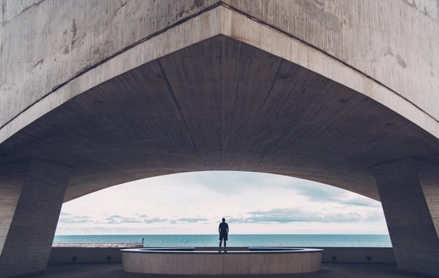 Vue arrière d'un homme debout sous un pont au bord de la mer