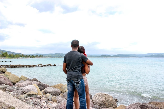 Vue arrière d'un homme et d'une femme debout au bord d'une rivière contre un ciel nuageux