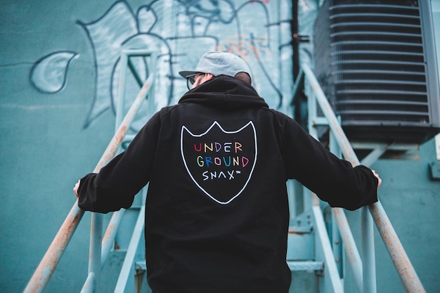 Vue arrière d'un homme hipster en capuchon noir debout sur un escalier en métal et détournant le regard.
